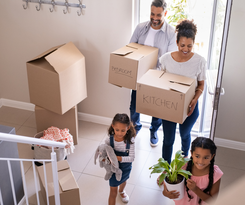 Man, woman and two children walking into new home with boxes, toys and plants